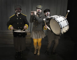 123 SCHTUNK - Ett drömspel (dekorativ bild på tre av skådespelarna som clowner med musikinstrument mot en mörk bakgrund)